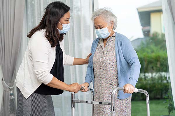 On Giving Tuesday, a woman wearing a face mask is kindly assisting an elderly woman with a walker.